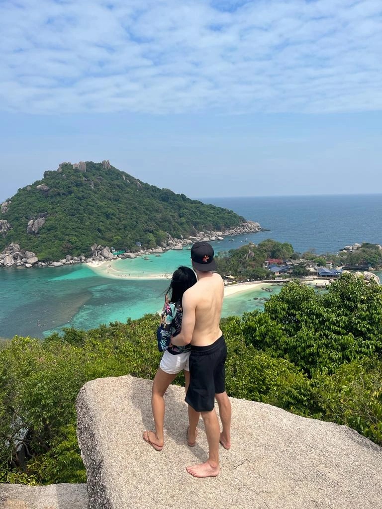 Ein junges Paar auf einer Insel auf einem hohen Felsen mit toller Aussicht aufs Meer und eine kleinere Insel in Thailand