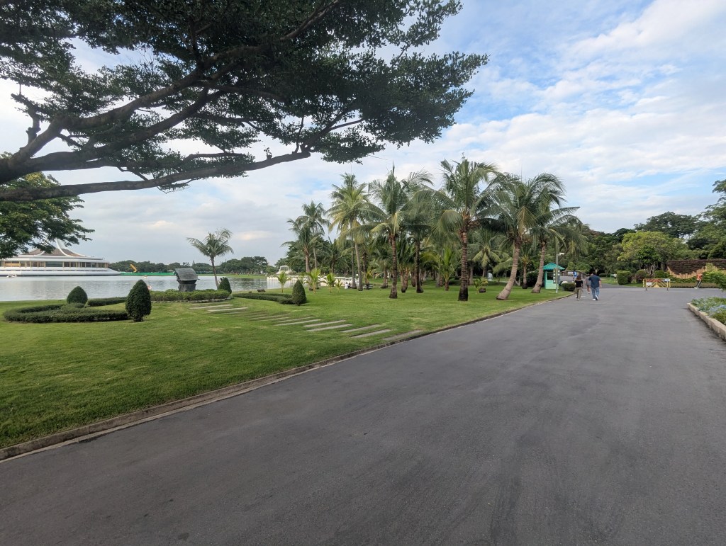 Asphaltierter Weg im Rama IX Park in Bangkok mit viel Pflanzen und Palmen