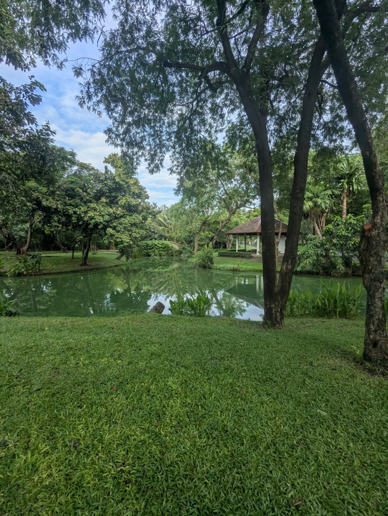 Gewässer im Grünen im Rama IX Park in Bangkok mit einem kleinen Haus im Hintergrund
